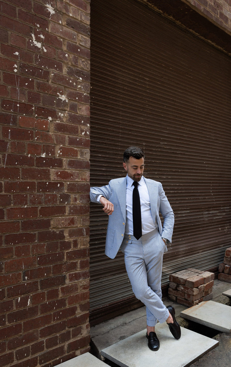 Man in a light gray suit leaning against a brick wall with a closed shutter.