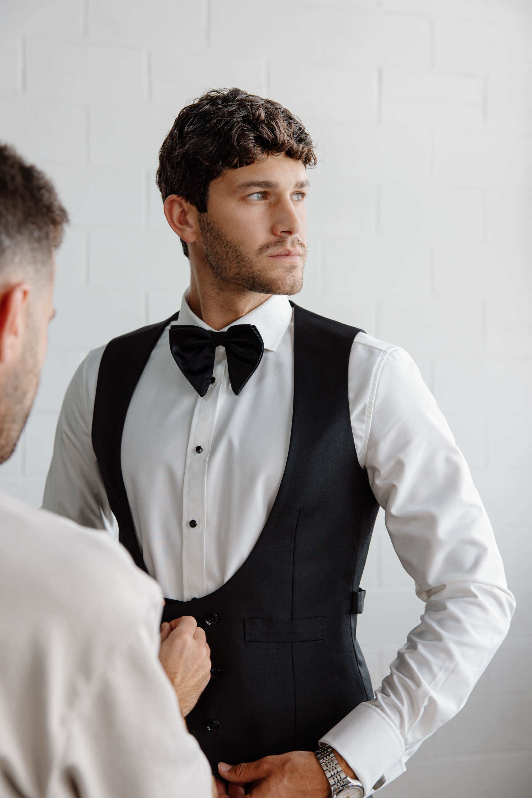 Man in a black tuxedo with a bow tie looking at himself in a mirror.