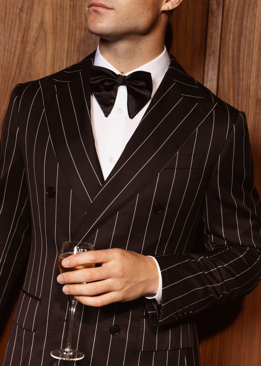 Close-up of The Tailors Lounge black double-breasted pinstripe suit with peak lapels, styled with a white shirt and black bow tie.